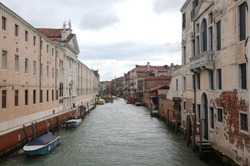 Houses and palaces overlooking large navigable canal with boats moored in Venice island in Italy