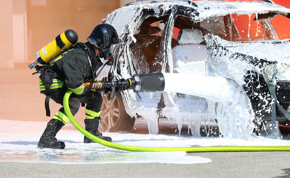 firefighter extinguishing a car fire with white foam extinguisher