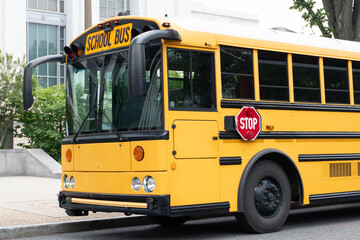 Iconic yellow school bus parked near educational building. Promotes safe transportation, learning access and American schooling system. Ideal for urban and educational content.