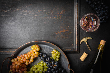 Wineglass with pink wine, fresh grapes and corks on dark wooden background with copy space