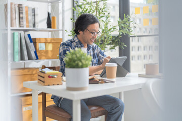 Cheerful Asian businessman with positive thinking and confidence sits at her desk, working in a modern home studio with her partners. he concentrates on their creative vision in the bright daylight