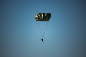 Paraquedista solitário descendo em silhueta contra um céu azul claro com espaço para texto
