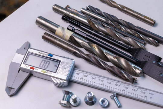 Collection of metal drill bits and measuring tools displayed on a white surface during a workshop session emphasizing precision and craftsmanship