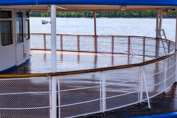 View of a spacious deck on a riverboat during a sunny day with calm water and greenery in the background