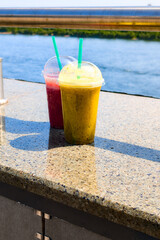 Refreshing smoothies in colorful cups enjoyed by the river on a sunny day during summer relaxation time