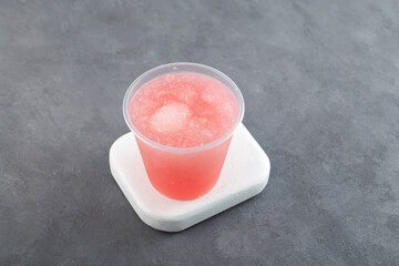 Flavored Shaved Ice or Frozen Slush Drink in disposable plastic cup, top view. Grapefruit pomelo granizado. Refreshing summer fruit drink. Street food take away
