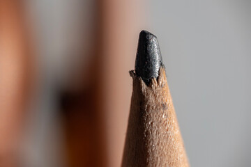 Extreme close-up of a sharpened pencil tip. The textured black graphite lead is exposed from the natural wood casing. The detailed grain of the wood is visible.