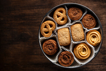 Crispy crumbly shortbread cookies in a round metal box on wooden table, top view, closeup, copy space