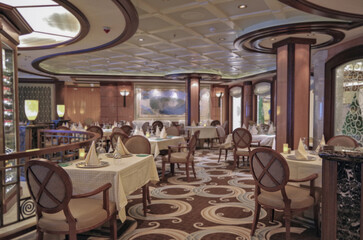 Formal and elegant ocean view dining room restaurant onboard luxury cruiseship or cruise ship liner with set tables in elegant Art Deco interior design style and ceiling ambient lighting