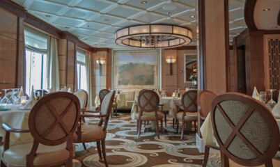Formal and elegant ocean view dining room restaurant onboard luxury cruiseship or cruise ship liner with set tables in elegant Art Deco interior design style and ceiling ambient lighting