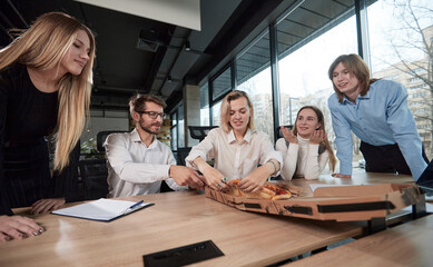 A group of people are sitting around a table with a pizza in the middle