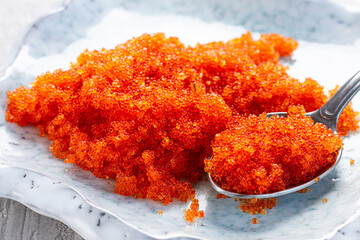 spoon with orange caviar, flying fish, Tobiko, on a light blue plate, caviar for rolls and sushi, close-up,