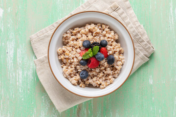 Pearl barley porridge with berries in a bowl on the table. Healthy breakfast. Top view