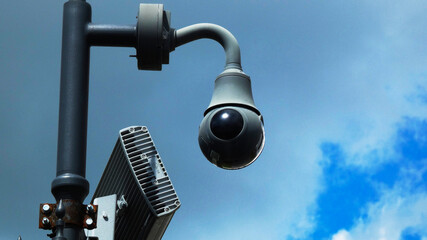 Security camera installed on a pole under a cloudy sky with visible technology in the background