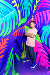 Boy posing with crossed arms in front of colorful tropical mural