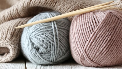 Knitting yarn balls and needles on a white wooden surface, with knitwear