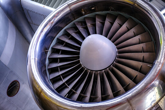 Close-up view of a jet engine turbine showcasing blue blades and a smooth metal casing in an aircraft maintenance facility