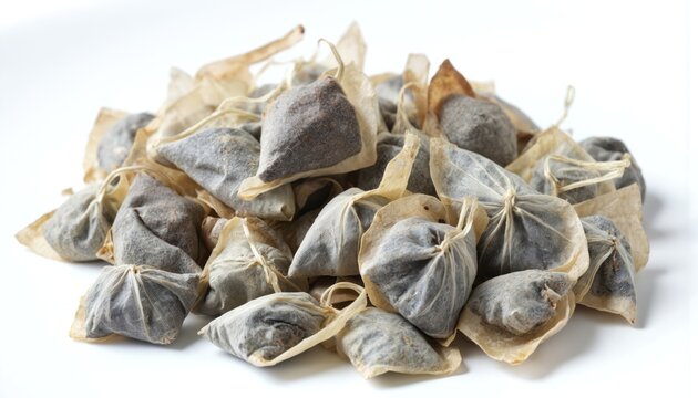 Collection of 15 black teabags in random scattered arrangement. Soft blurred gray background. Elevated perspective makes teabags appear to float. No pattern organization. Suggests dry, isolated,