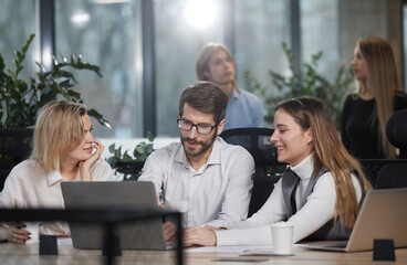 Three people are sitting around a table with laptops