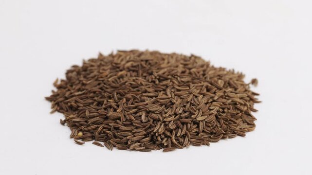 Caraway seeds rotating slowly on white background, showing natural shape and earthy color.
