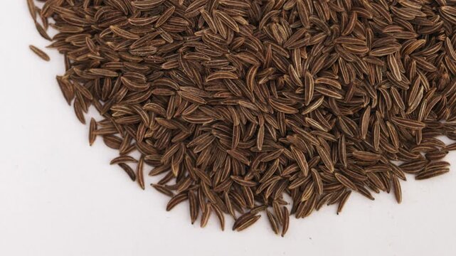 Caraway seeds rotating slowly on white background, showing natural shape and earthy color.