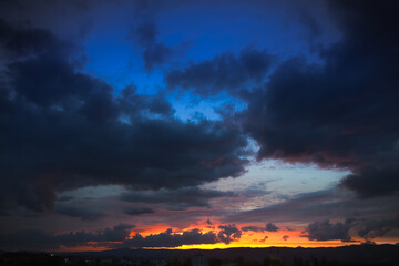 A dramatic sunset with dark, brooding clouds covering the top half of the sky and a fiery orange and yellow sunset at the bottom.