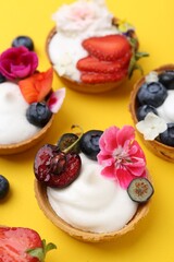 Sweet tartlets with berries and flowers on yellow background, above view. Delicious dessert