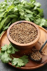 Coriander seeds in bowl, spoon and fresh cilantro leaves on dark table, closeup