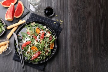Tasty salad with arugula, cheese, grapefruit, vegetable and balsamic sauce served on dark wooden table, flat lay. Space for text