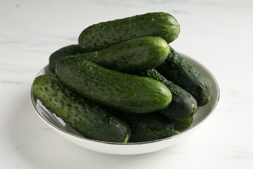 Fresh cucumbers in bowl on white table, closeup