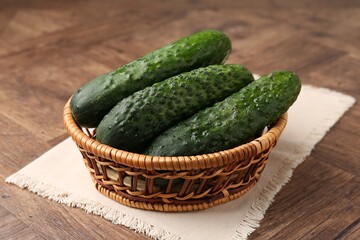 Fresh cucumbers in wicker basket on wooden table, closeup