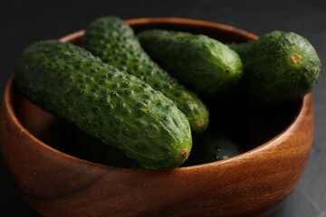 Fresh cucumbers in bowl on dark table, closeup