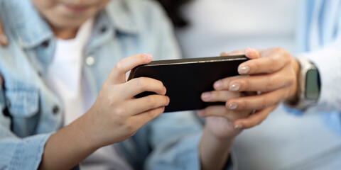 Close Interaction. Child and parent holding smartphone together, focused on screen.