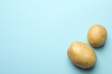 Fresh raw potatoes on light blue background, space for text