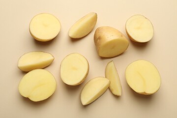 Cut raw potatoes on beige background, above view