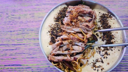 Grilled chicken slices served over noodles with creamy cheese sauce and seasoning in a metal bowl. The image represents fusion cuisine, indulgent comfort food and modern Korean-style street dining