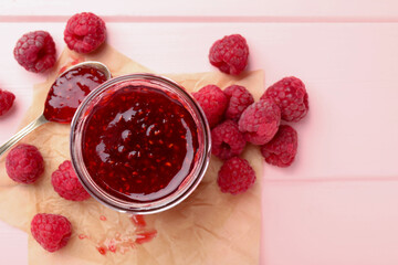 Sweet raspberry jam in glass jar and berries on pink wooden table, flat lay