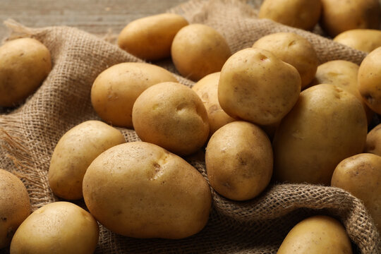 Many raw potatoes and burlap fabric on table, closeup