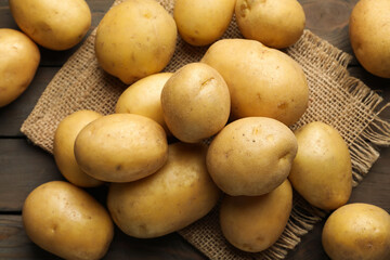 Many raw potatoes and burlap fabric on wooden table, flat lay