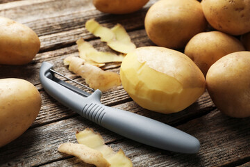 Many raw potatoes and peeler on wooden table, closeup