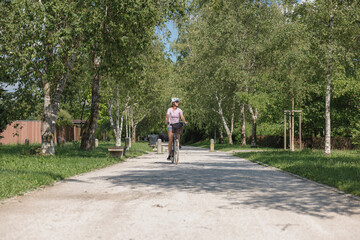 Fototapeta premium A cyclist rides along a scenic pathway surrounded by lush trees and greenery on a sunny day, enjoying the outdoors and fresh air.
