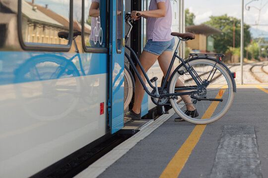 A cyclist prepares to board a train with a bicycle at a busy station during daytime, showcasing sustainable transport.