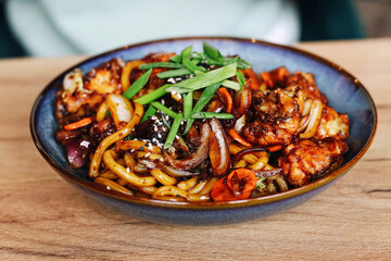 Asian stir fry noodles. Chicken with vegetables and sauce. Freshly served dish in bowl. Delicious meal with green onions. Traditional Asian food on wooden table. Tasty lunch or dinner option.