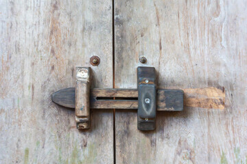 A wooden lock with a bolt and metal screws on a weathered wooden door. The vintage look creates a rustic and authentic effect.