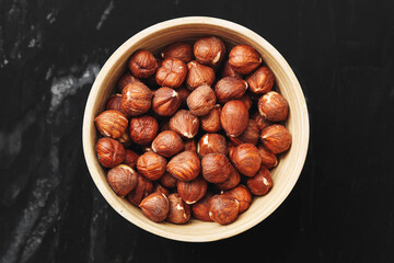 Raw hazelnuts in bowl. Brown nuts on black background. Healthy organic food. Natural snack or baking ingredient. Rustic composition for kitchen. Protein rich and nutritious nuts for health.