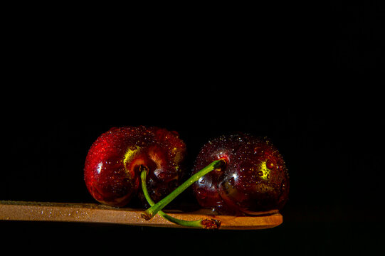 Primer plano de dos cerezas rojas con escarcha encima de una cuchara de madera