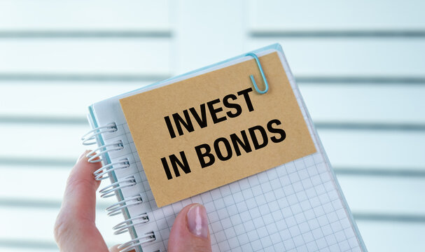 A person is holding a notebook with the word Invest in Bonds written on it.