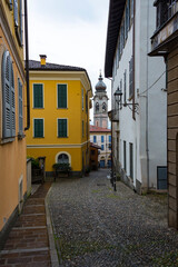 A narrow road paved with round stones, old buildings with shutters and church in a gap between them in Menaggio, Lombardia, Italy