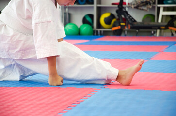 Young Kyokushin karate student performing a side split stretch on dojo mat, wearing a traditional...