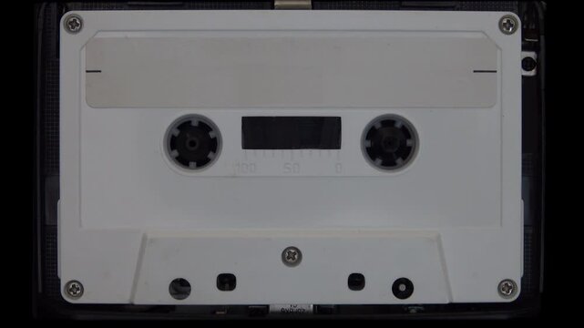 An unlabeled, white analog cassette tape with an blank label plays in a closeup view, shown in real time.
